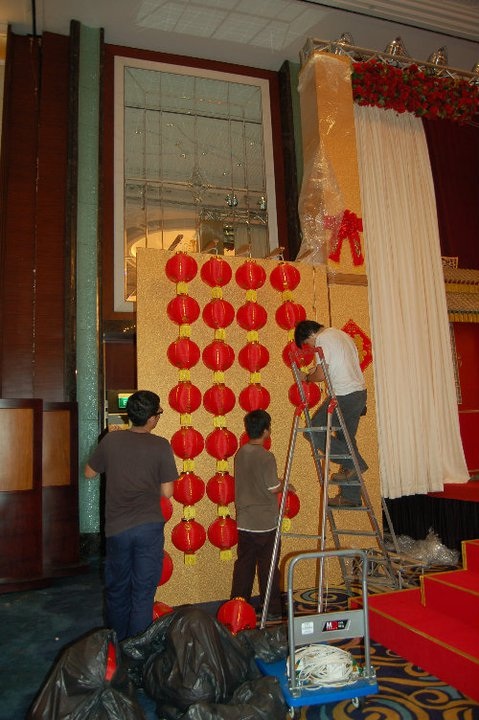 Three individuals collaborating to set up a red lantern decorative backdrop.