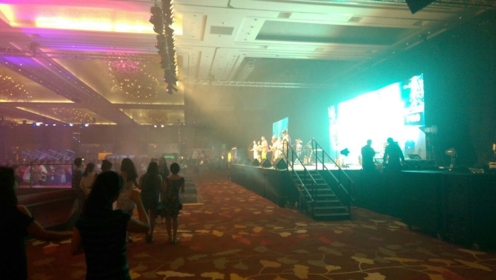 A vibrant indoor event featuring a brightly lit stage with large screens displaying dynamic visuals.