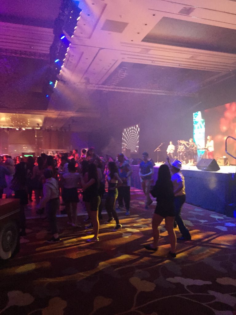 A live music performance featuring a band on stage under vibrant, colorful lighting.