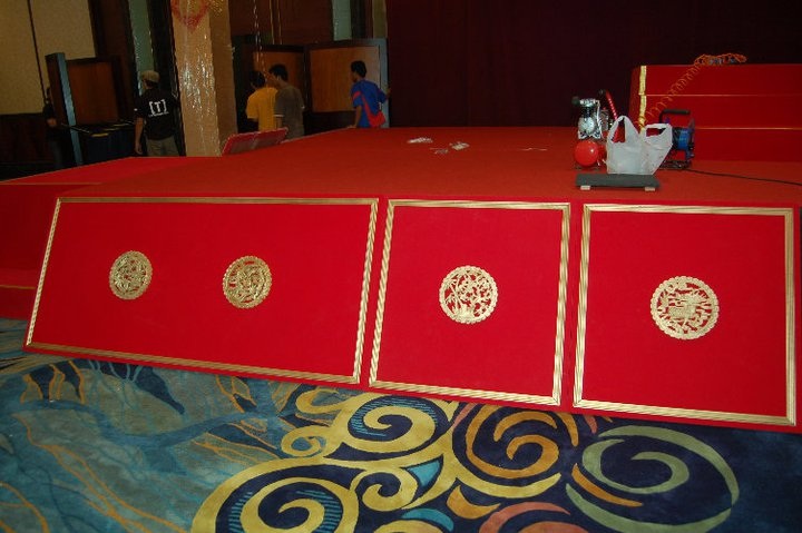 A stage setup featuring three red panels with intricate golden designs framed in gold.