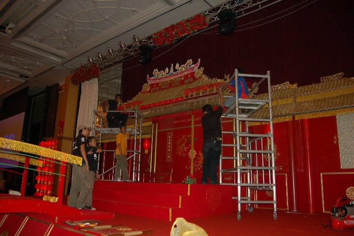 A group of individuals working together to set up an elaborate red and gold decorative structure indoors