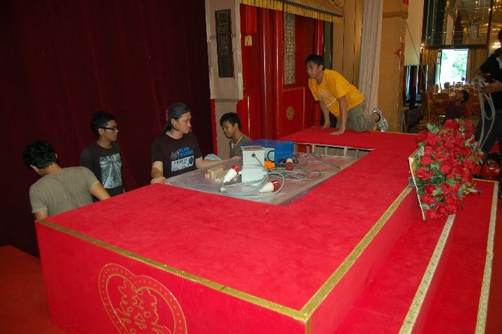 A group of five individuals collaborates on a stage platform draped in red with a striking golden border.