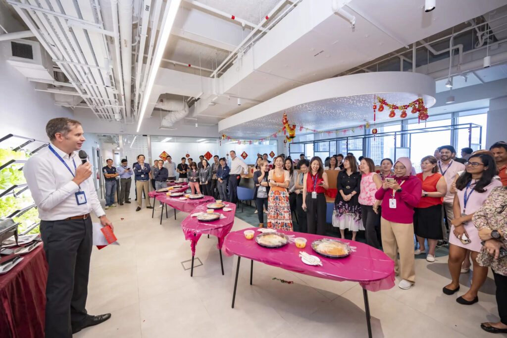 Colleagues gather in their office for a corporate event with food and a speaker, illustrating how utilizing internal venue space is a budget-friendly strategy.