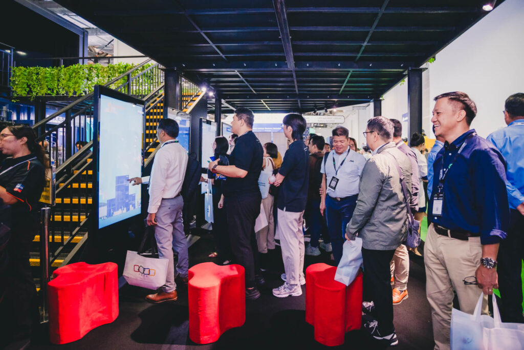 Visitors interacting with a large digital touchscreen at the Mitsubishi Heavy Industries innovation booth during a trade show