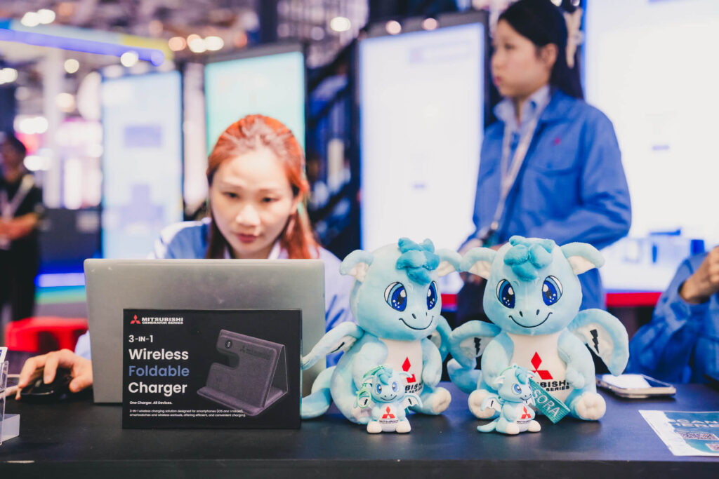 Mitsubishi 'Sora' dragon mascot plushies and branded wireless chargers displayed at the MHI-ESA innovation booth