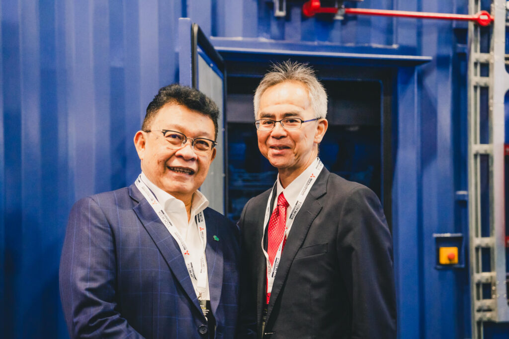 Two business professionals posing at the Mitsubishi Heavy Industries booth during an industrial exhibition