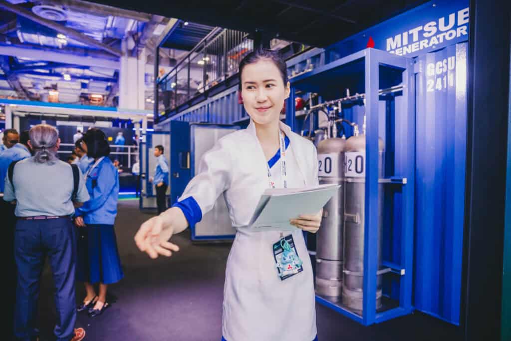 A friendly Mitsubishi Heavy Industries staff member welcoming visitor to the innovation booth at a data center exhibition