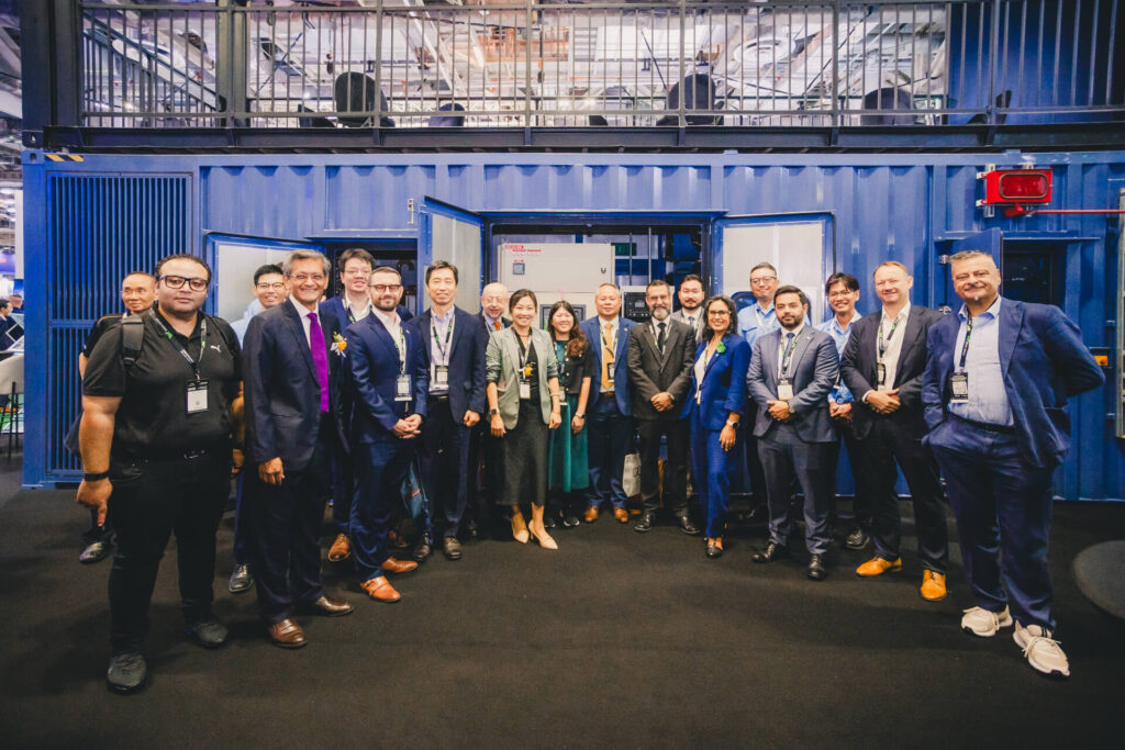 A group photo of MHI-ESA staff and partners in front of the MGS2500R containerized generator at Data Centre World Asia 2025